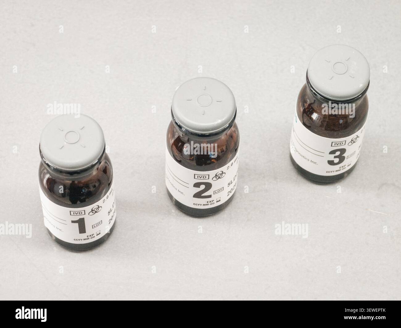 Drei braune Glas-Diagnosepipetten mit den Etiketten 1, 2 und 3 liegen auf einer hellen Oberfläche, jede mit Biohazard-Symbolen, IVD-Kennzeichnung, Volumendaten und einer - Smartphone-aufgenommenes Stockfoto
