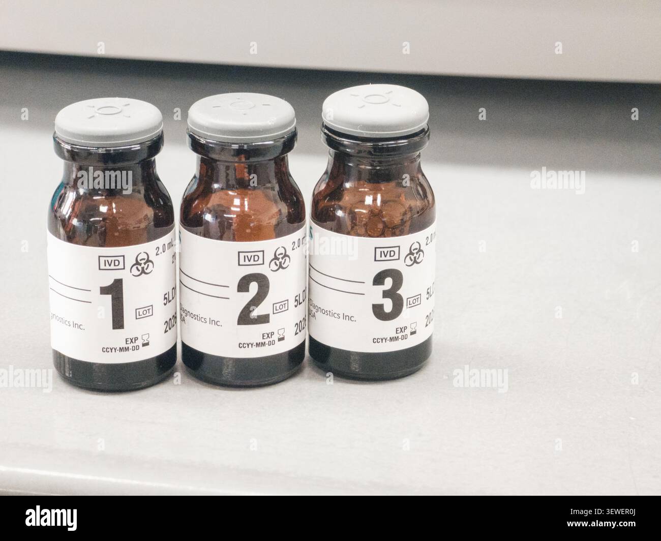 Drei braune Glas-Diagnosepipetten mit den Etiketten 1, 2 und 3 liegen auf einer hellen Oberfläche, jede mit Biohazard-Symbolen, IVD-Kennzeichnung, Volumendaten und einer - Smartphone-aufgenommenes Stockfoto