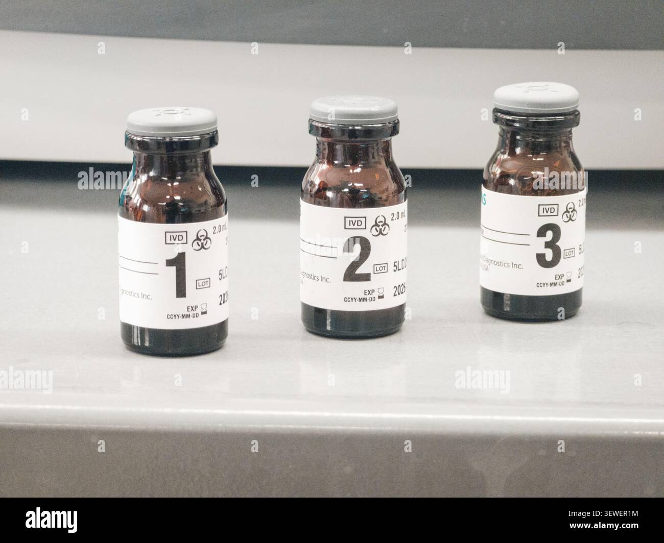 Drei braune Glas-Diagnosepipetten mit den Etiketten 1, 2 und 3 liegen auf einer hellen Oberfläche, jede mit Biohazard-Symbolen, IVD-Kennzeichnung, Volumendaten und einer - Smartphone-aufgenommenes Stockfoto