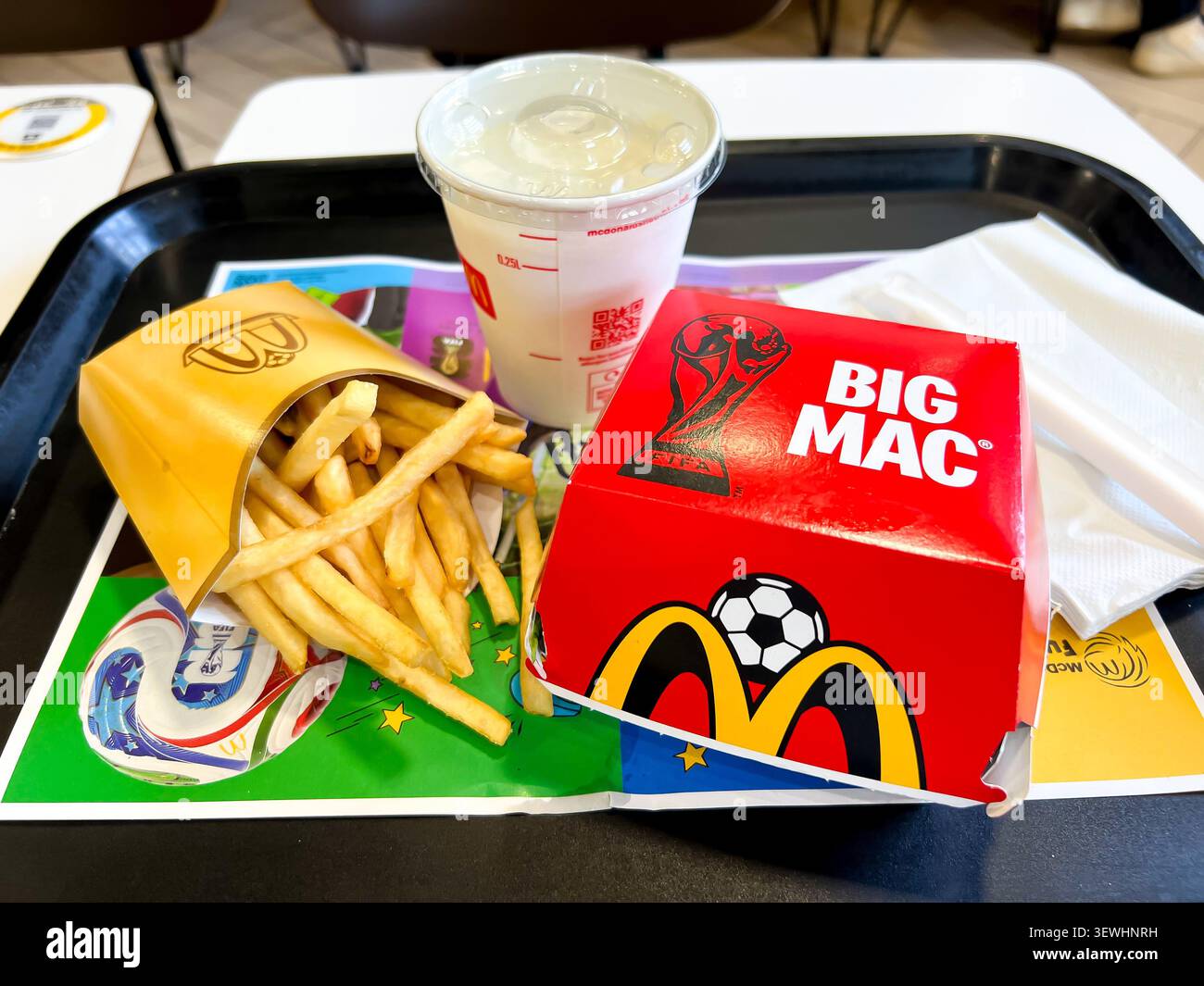 Nahaufnahme einer mittelgroßen Portion McDonalds Pommes und eines Big Mac Hamburger in spezieller World Cup Verpackung mit Bananenmilkshake zum Mittagessen - Smartphone-aufgenommenes Stockfoto