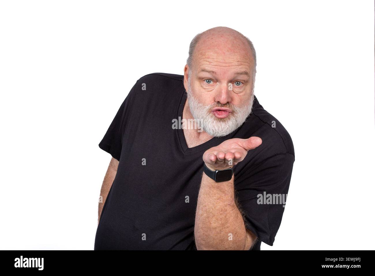 Bärtiger Mann mittleren Alters, der einen Kuss in schwarzem Hemd mit generischer Armbanduhr auf weißem Hintergrund bläst Stockfoto