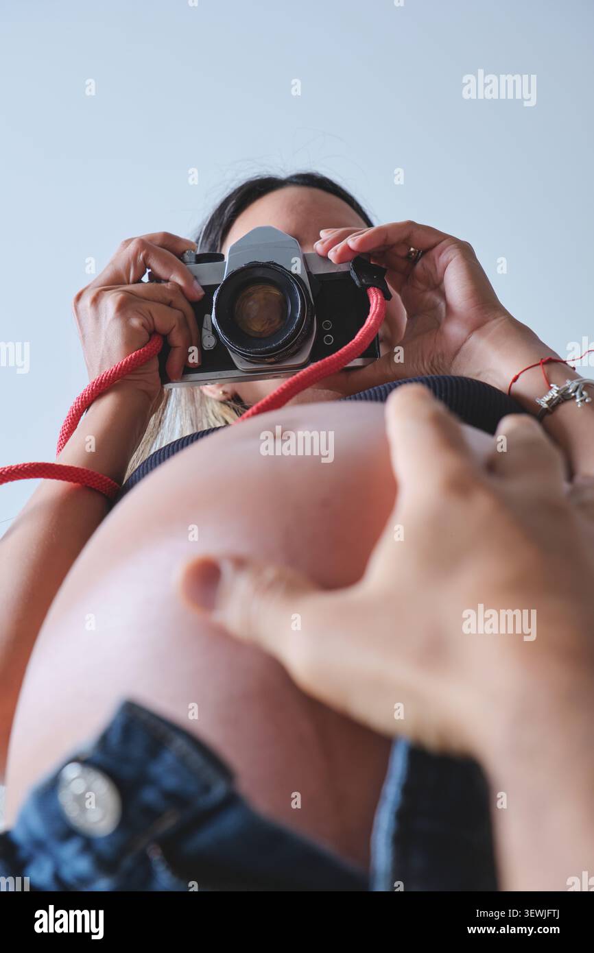 Eine Frau, die Kamera über ihren schwangeren Bauch hält, die Hand eines Mannes berührt die Beule Stockfoto