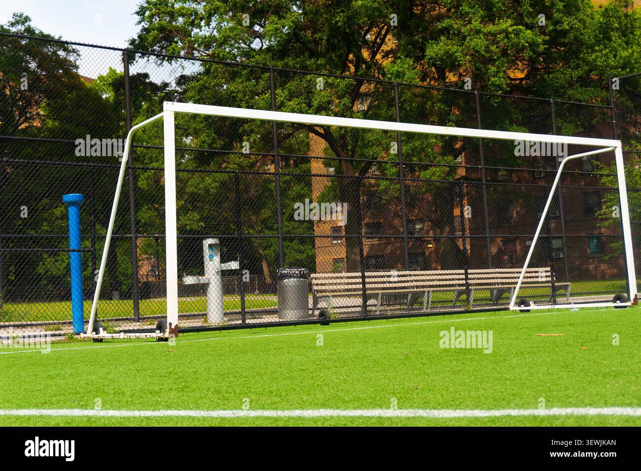 Ein ruhiges Fußballfeld mit Torpfosten auf grünem Rasen, umgeben von einem Zaun und Bäumen. Stockfoto