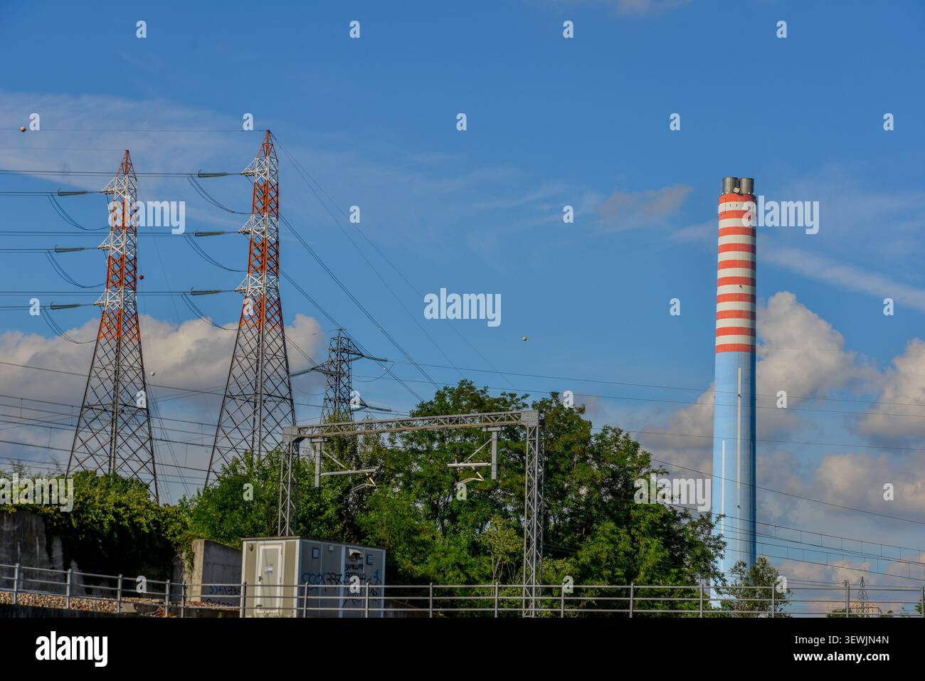 Industrie- und Infrastrukturpanorama an einem klaren Tag. Auf der linken Seite stehen zwei große Hochspannungsmasten, gekennzeichnet durch Wechselwirkungen Stockfoto