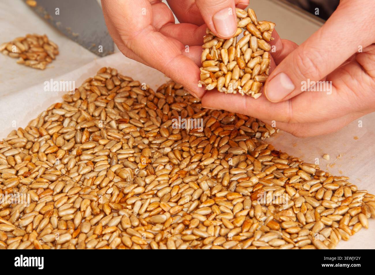 Eine Person bricht ein Stück frisch gemachtes Sonnenblumenkorn aus einer größeren Platte ab Stockfoto