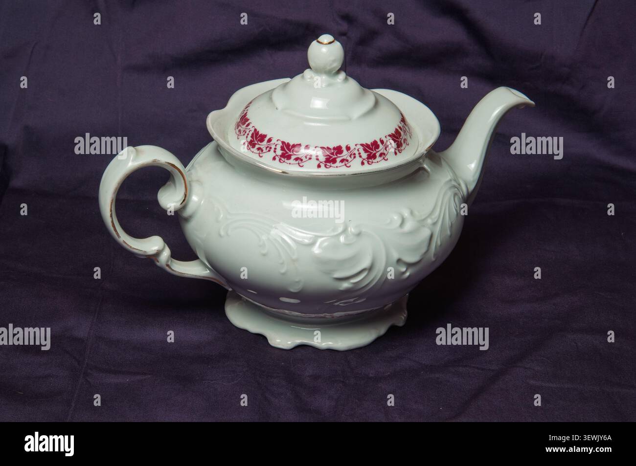 Elegante antike Porzellan-Teekanne mit kunstvollen Reliefdetails und zartem rotem Blumenrand Stockfoto