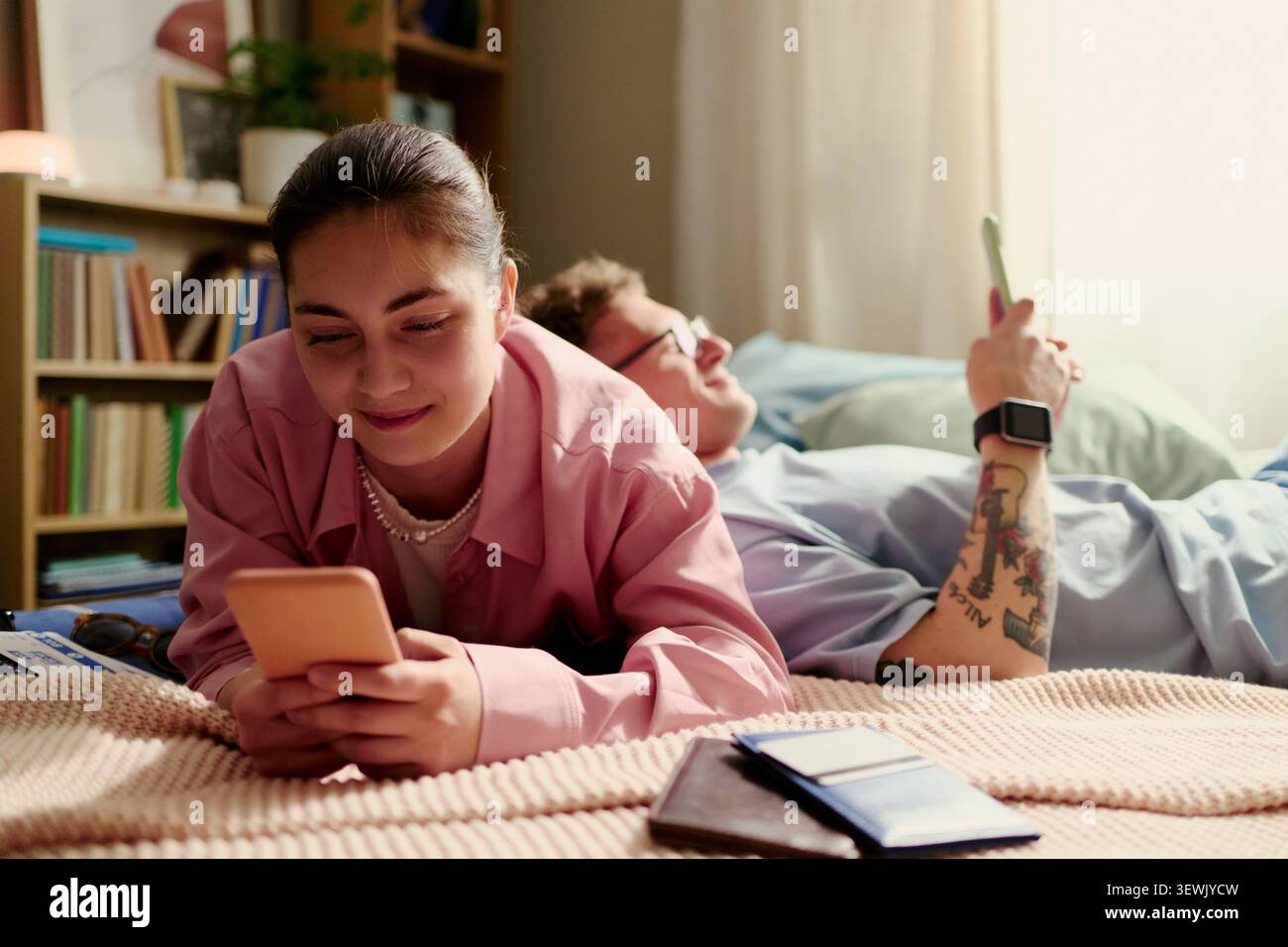 Junge Erwachsene Paare, die Smartphones benutzen, während sie sich auf den Urlaub zu Hause vorbereiten, Reiseinformationen und Tickets prüfen. Ideal für Tourismusplanung, mobile Buchungen, Lifestyle-Marketing für Paare Stockfoto