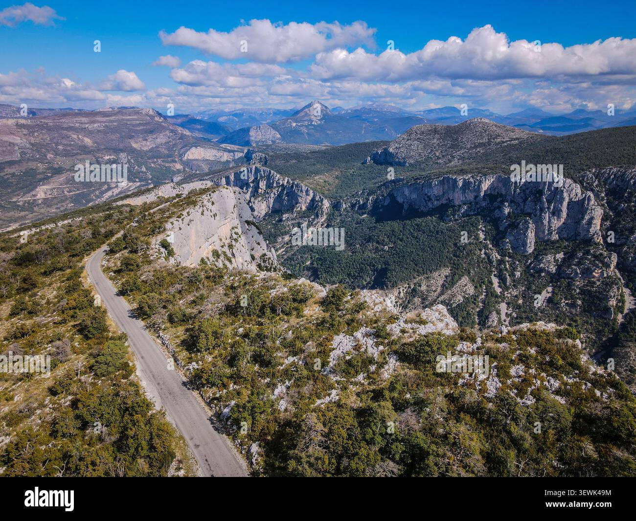 Eine Rundfahrt aus der Vogelperspektive zeigt eine gewundene Asphaltstraße, die durch zerklüftetes, felsiges Gelände mit dünner Vegetation führt. Im Hintergrund, majestätisch Stockfoto
