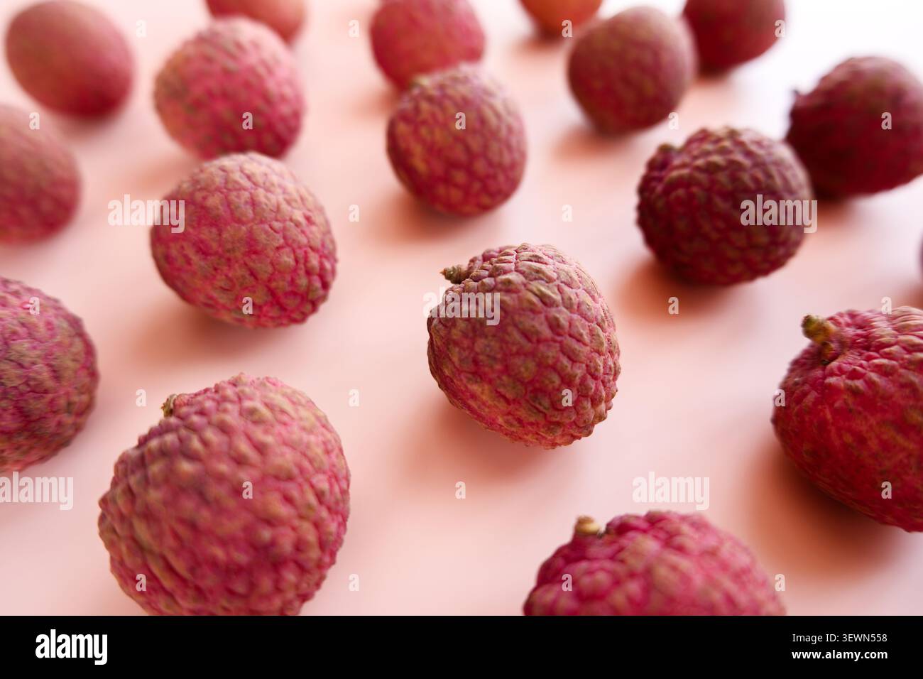 Frische Litschi-Früchte auf weichem rosa Hintergrund, Nahaufnahme mit flachem Fokus. Helles tropisches Lebensmittelbild mit natürlicher Textur, Kopierraum und Stockfoto