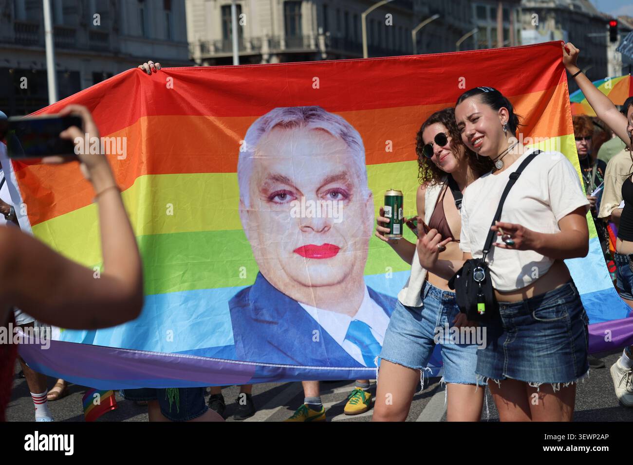 Die Leute posieren mit einem Regenbogenbanner mit dem Gesicht des ehemaligen ungarischen Premierministers Viktor Orban, der während des Budapester Pride march Make-up trägt Stockfoto