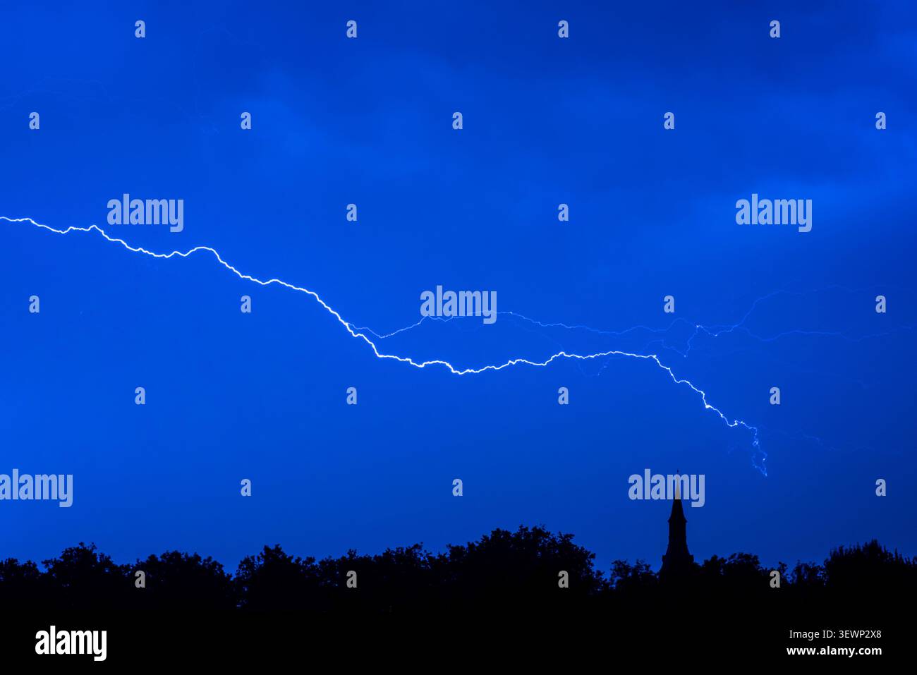 Blitzschlag / Blitzschlag innerhalb der Wolke während eines Gewitters am blauen Nachthimmel über Wald mit Silhouetten und Kirchturm, Mari Stockfoto