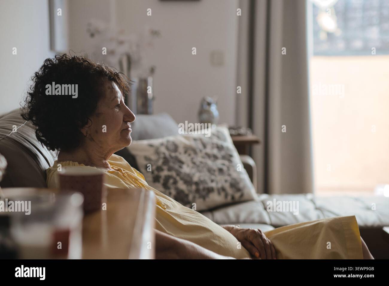 Einsame ältere abhängige Frau, die allein auf der Couch zu Hause sitzt und an Krankheit oder Demenz leidet Stockfoto