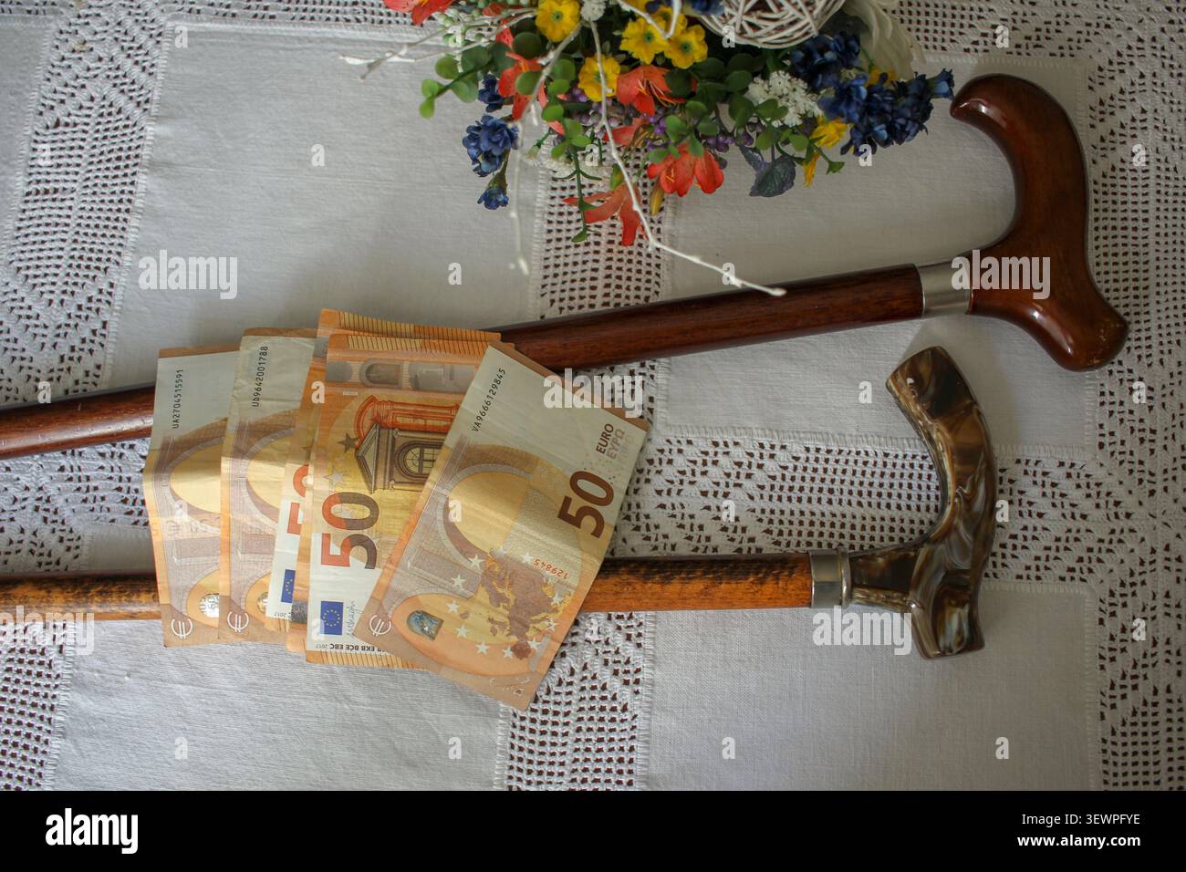 Eine konzeptionelle Top-down-Aufnahme von mehreren 50 Euro-Scheinen, die über zwei Vintage-Gehstöcken auf einer weißen Tischdecke platziert wurden, die Seniorenrenten repräsentieren Stockfoto