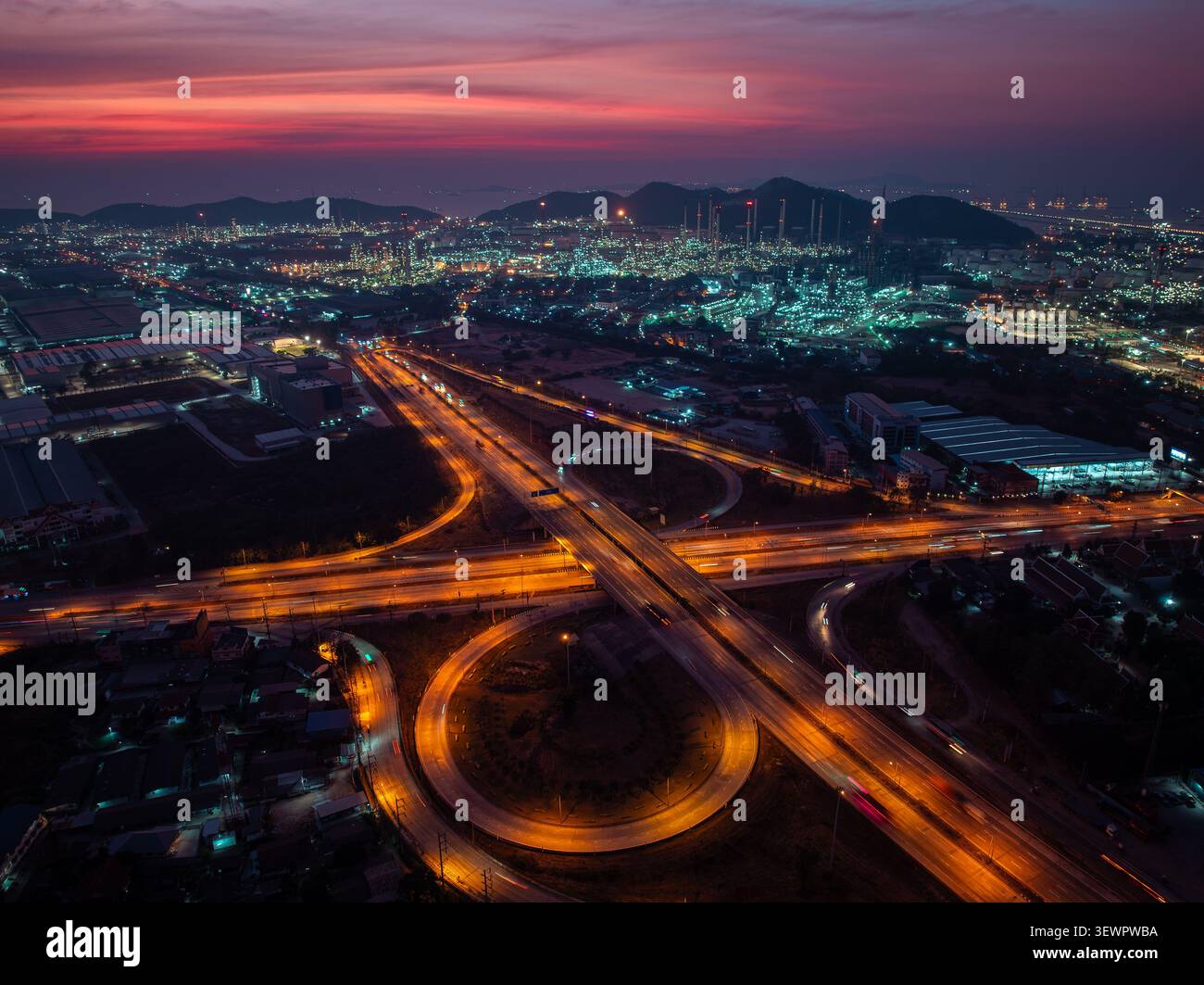 Eine Langzeitbelichtung bei Nacht eines Autobahnkreuzes, der städtische Gebiete mit der Infrastruktur der industriellen Raffinerie bei Sonnenuntergang in laem chabang thailand verbindet. Stockfoto