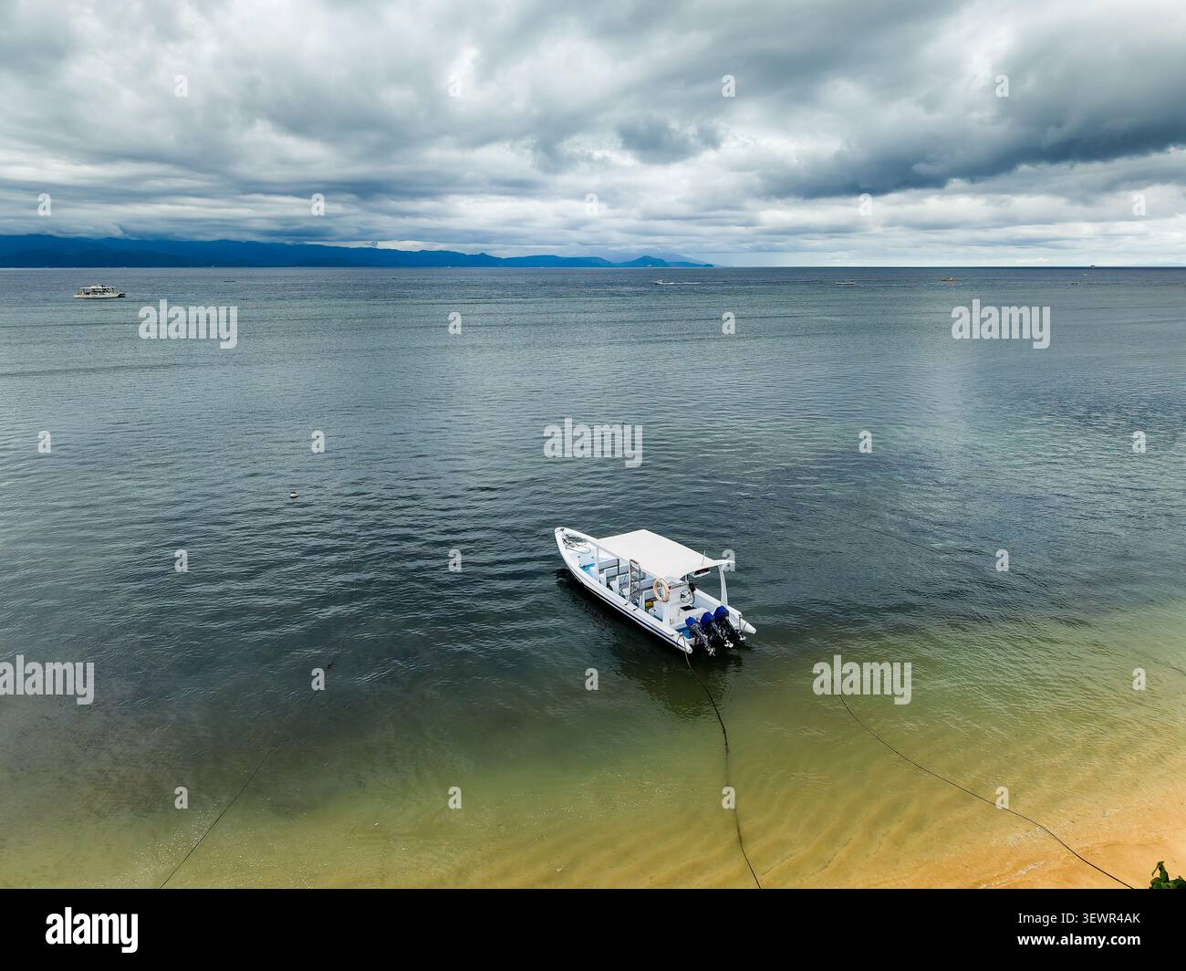 Blick aus der Höhe auf ein weißes Motorboot, das in ruhigem, flachem Wasser in der Nähe des Ufers verankert ist Stockfoto