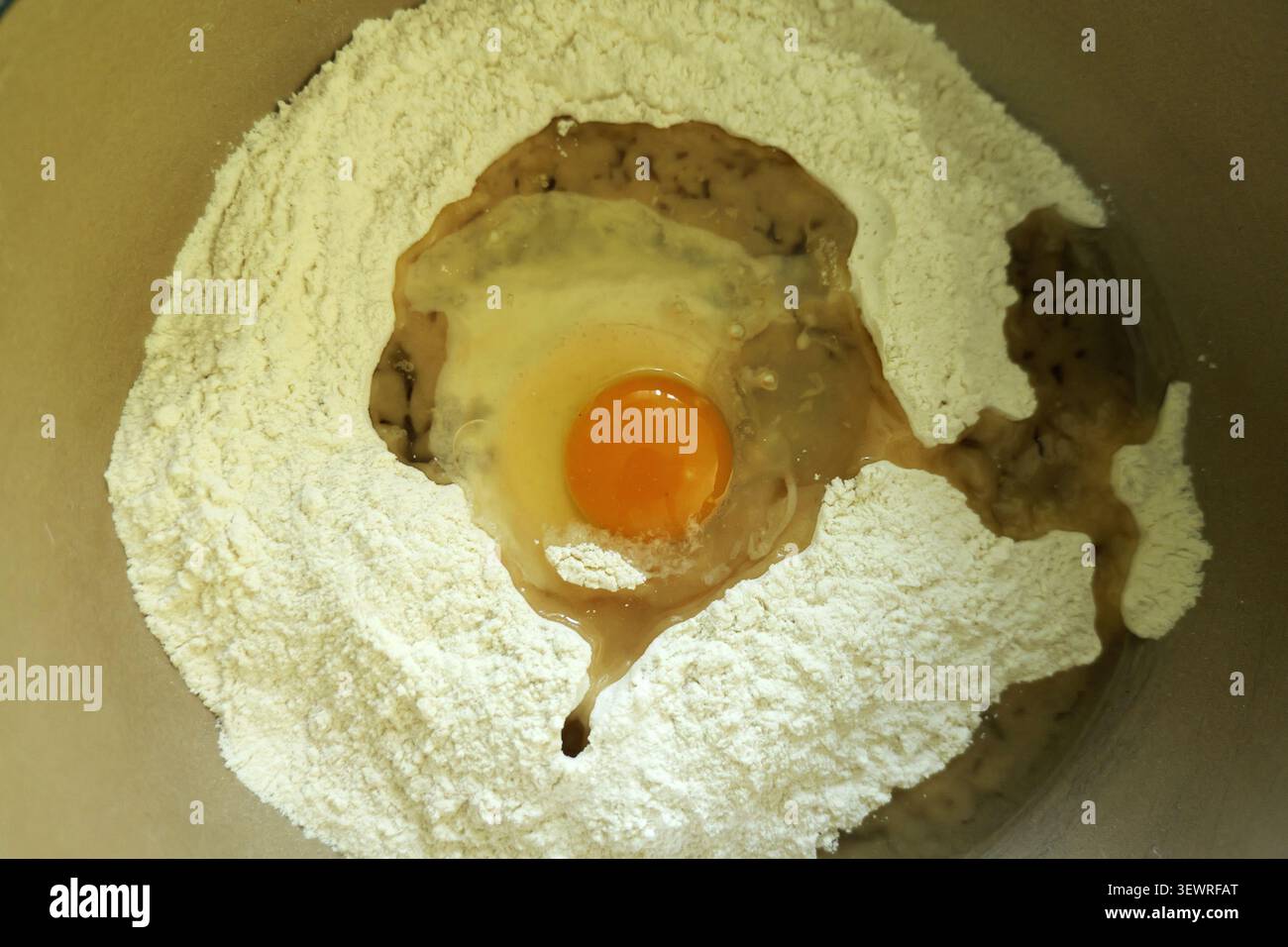 Mehl, rohes Ei und flüssige Zutaten werden in einer Schüssel gemischt, um die wesentlichen Schritte der Teigzubereitung zum Backen oder Kochen darzustellen Stockfoto