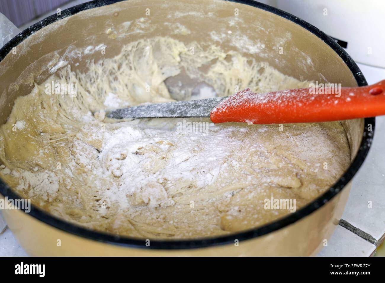 Brotteig, mit Mehl bestreut und mit glutenbildenden Fäden versehen, liegt in einer Schüssel mit einem Teigschaber und bereitet den hausgemachten Bakin vor Stockfoto