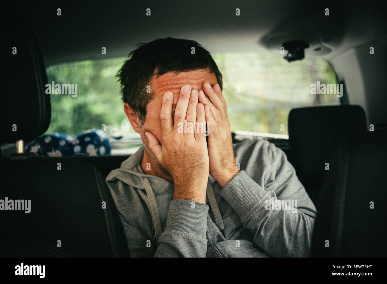 Ein Mann mittleren Alters sitzt in einem Auto mit dem Kopf auf der Hand, erscheint müde, gestresst und tief in Gedanken. Selektiver Fokus. Stockfoto