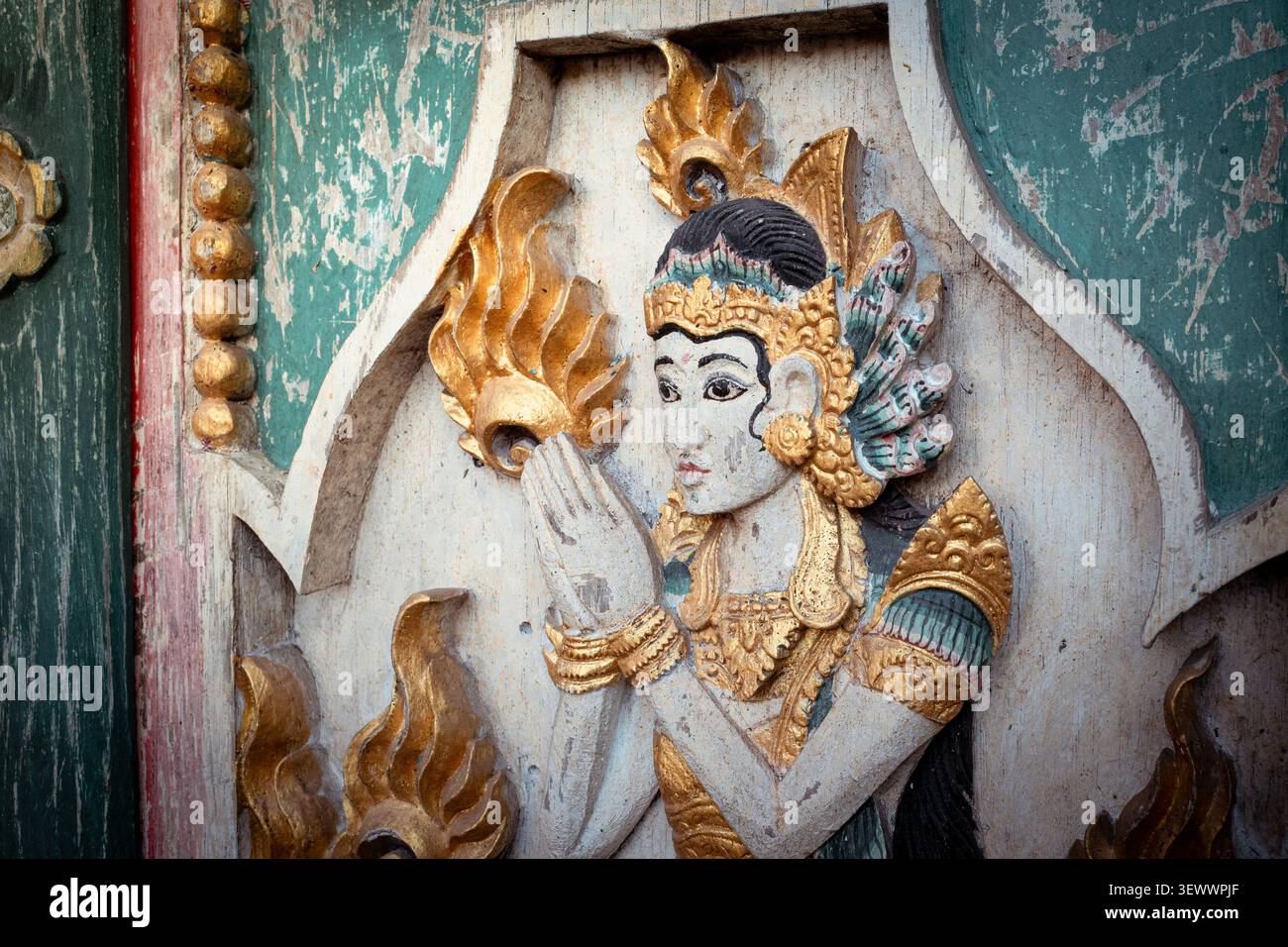 Balinesische traditionelle Holzschnitzerei, die eine weibliche Gottheit oder Göttin mit Händen in Gebetshaltung zeigt, verziert mit Blattgold und alten lebendigen Farben an einer Hindutempel-Tür Stockfoto