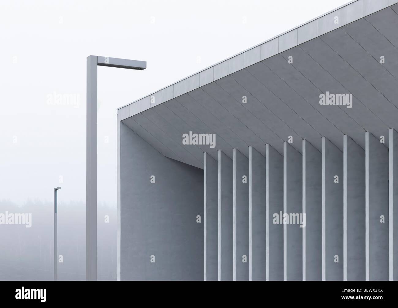 Minimales Betongebäude mit vertikalen Säulen und Straßenlaternen in nebeliger städtischer Umgebung. Geometrische Struktur mit sich wiederholenden Elementen und archit Stockfoto