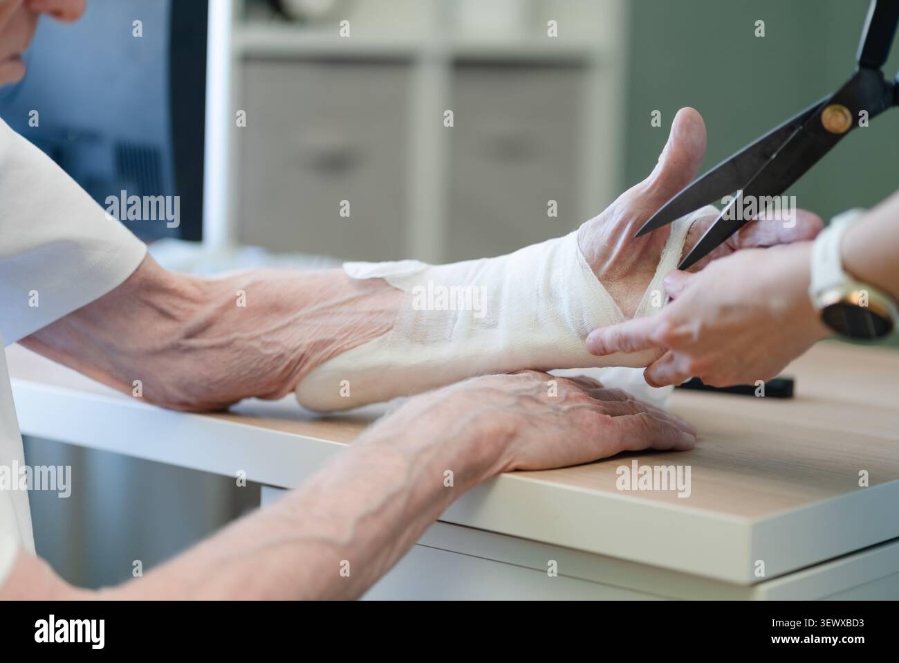 Pflegefachverband ältere Männerhand mit Knochenfragilitätskrankheit im klinischen Umfeld. Medizinisches Fachpersonal, das eine präzise Wundversorgung bei älteren Patienten mit altersbedingten Erkrankungen anwendet Stockfoto