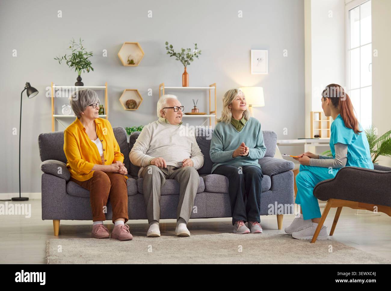 Gruppe von Senioren, die mit einer jungen Krankenschwester auf Sofa sitzen. Stockfoto