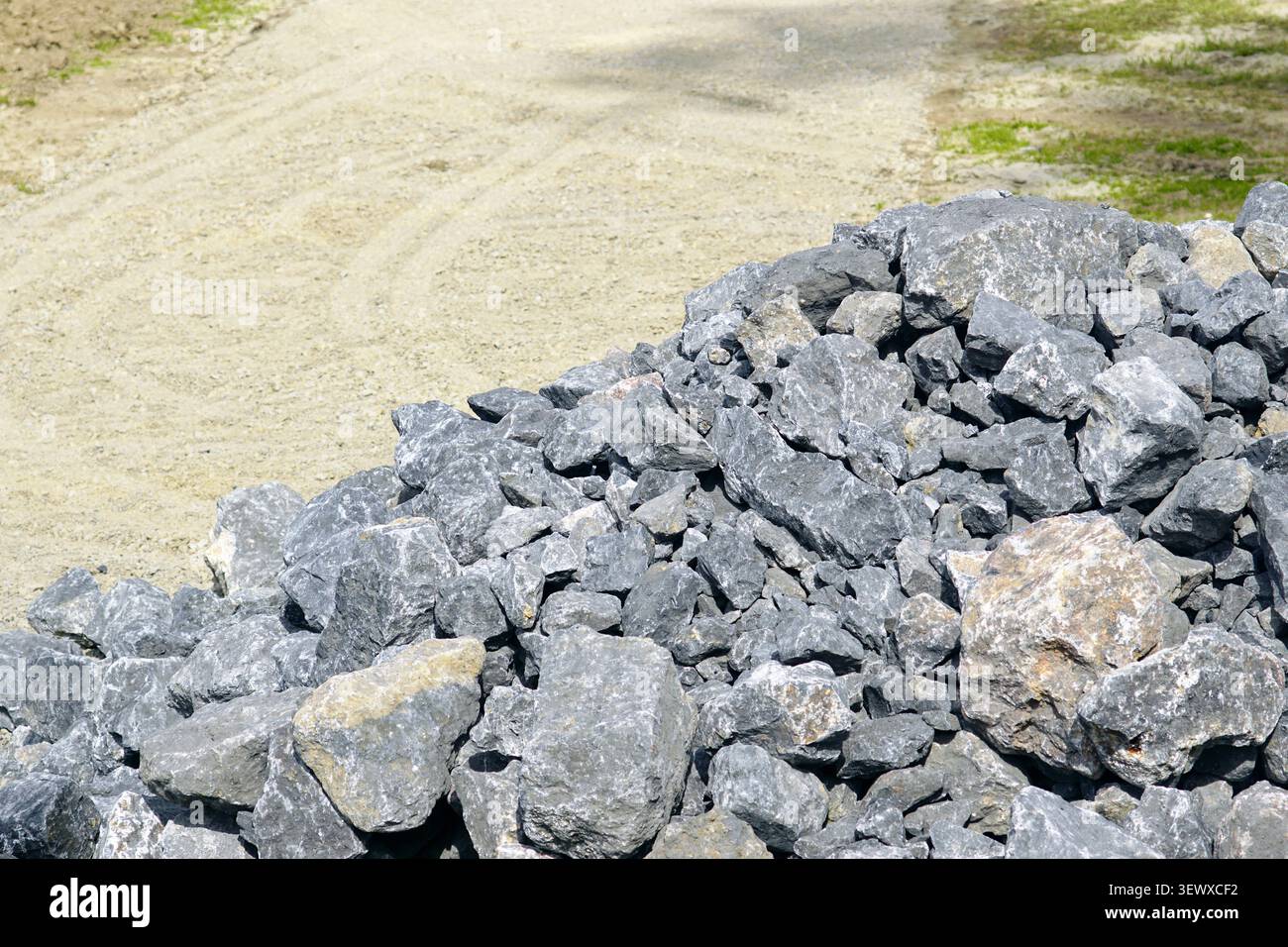 Bruchsteine neben einer aktiven Baustraße gelagert, die auf die zukünftige Installation warten. Langlebige Infrastrukturplanung und lebensdauerorientierte Ingenieurskunst Stockfoto