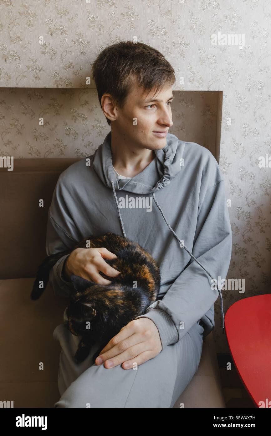 Junger Mann, der auf dem Sofa sitzt und Schildpattkater hält Stockfoto