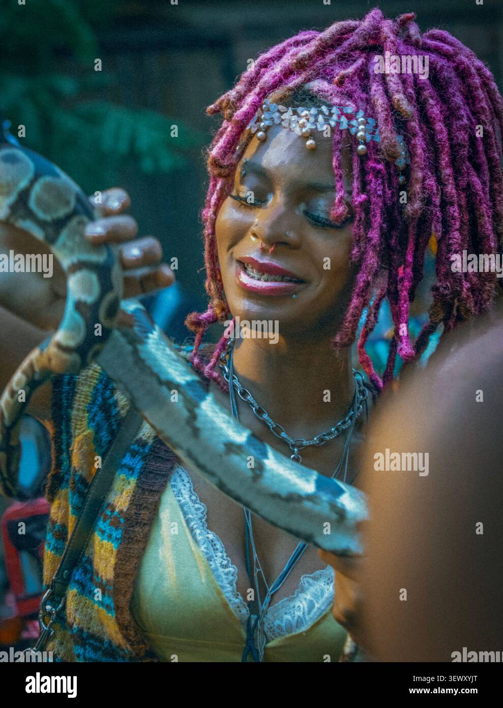 Glückliche Frau mit rosa Dreadlocks, die eine Schlange hält Stockfoto