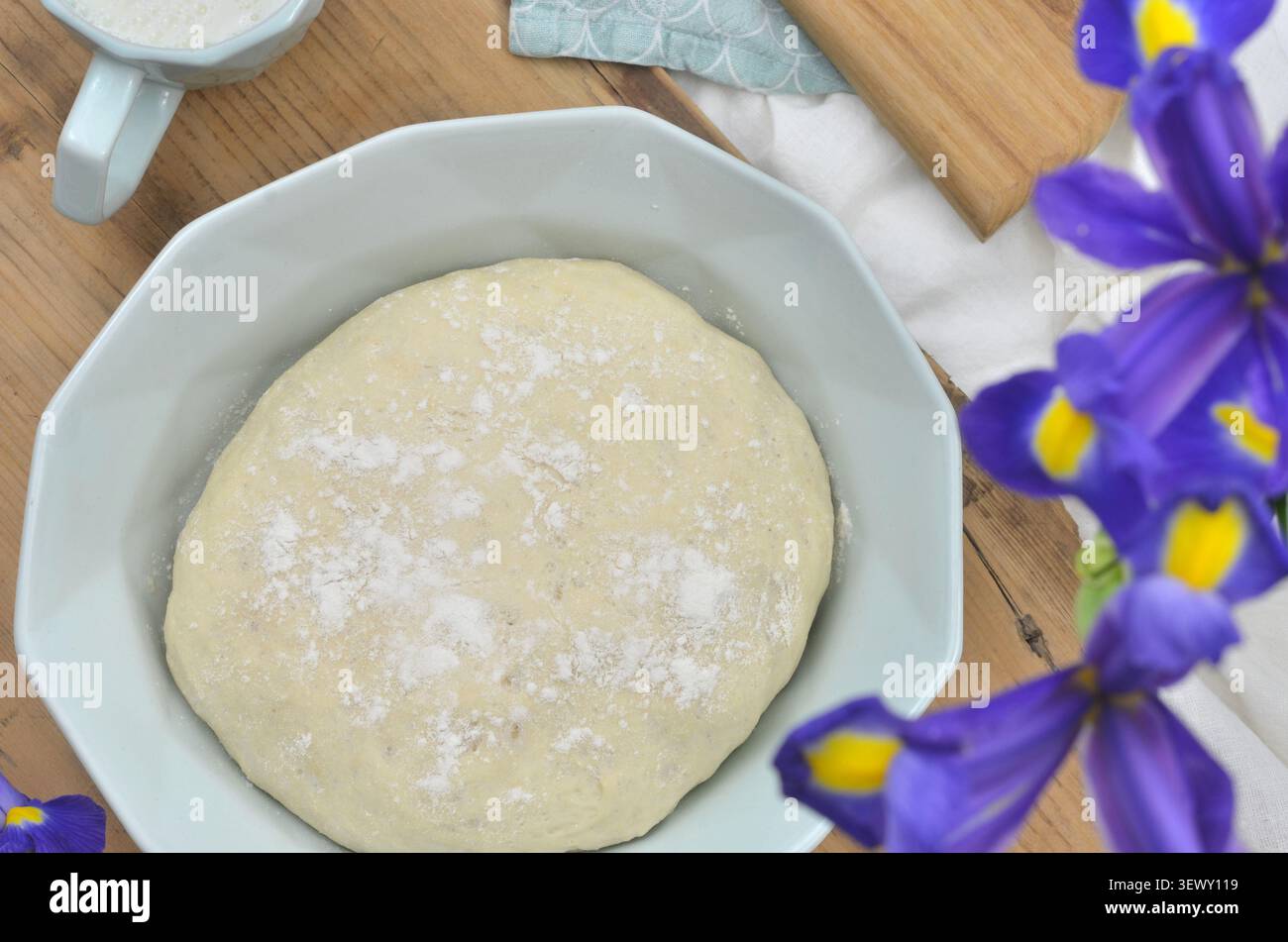 Roher Hefeteig in einer Minzschale auf einem Holztisch. Minzschmuck und violette Blumen. Hefeteig wird für Brot, Brötchen, Pita, Pizza oder Kuchen verwendet. Stockfoto
