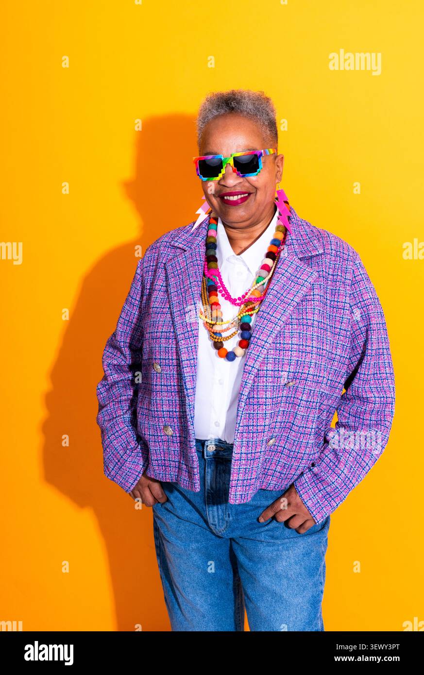 Schwarze ältere Frau trägt moderne Kleidung Porträt auf Hintergrund - ältere afroamerikanische Frau in bunten Pixel Sonnenbrillen und mehrschichtigen Halsketten, s Stockfoto