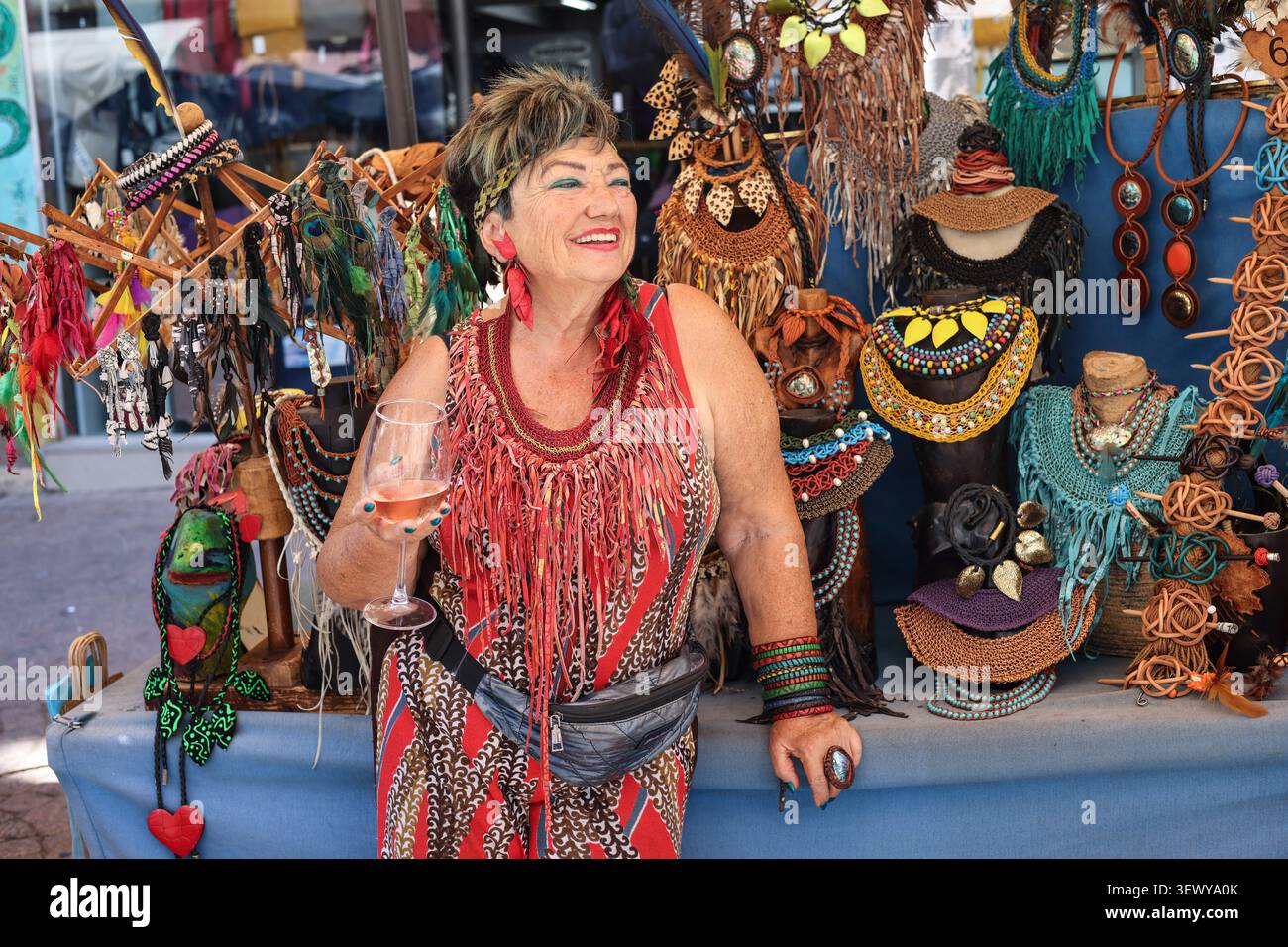 TEL AVIV, ISRAEL - 22. September 2023: Ein lächelnder Verkäufer hält ein Glas Wein an ihrem farbenfrohen Schmuck- und Accessoires-Stand auf der Nachalat Binyamin Stree Stockfoto
