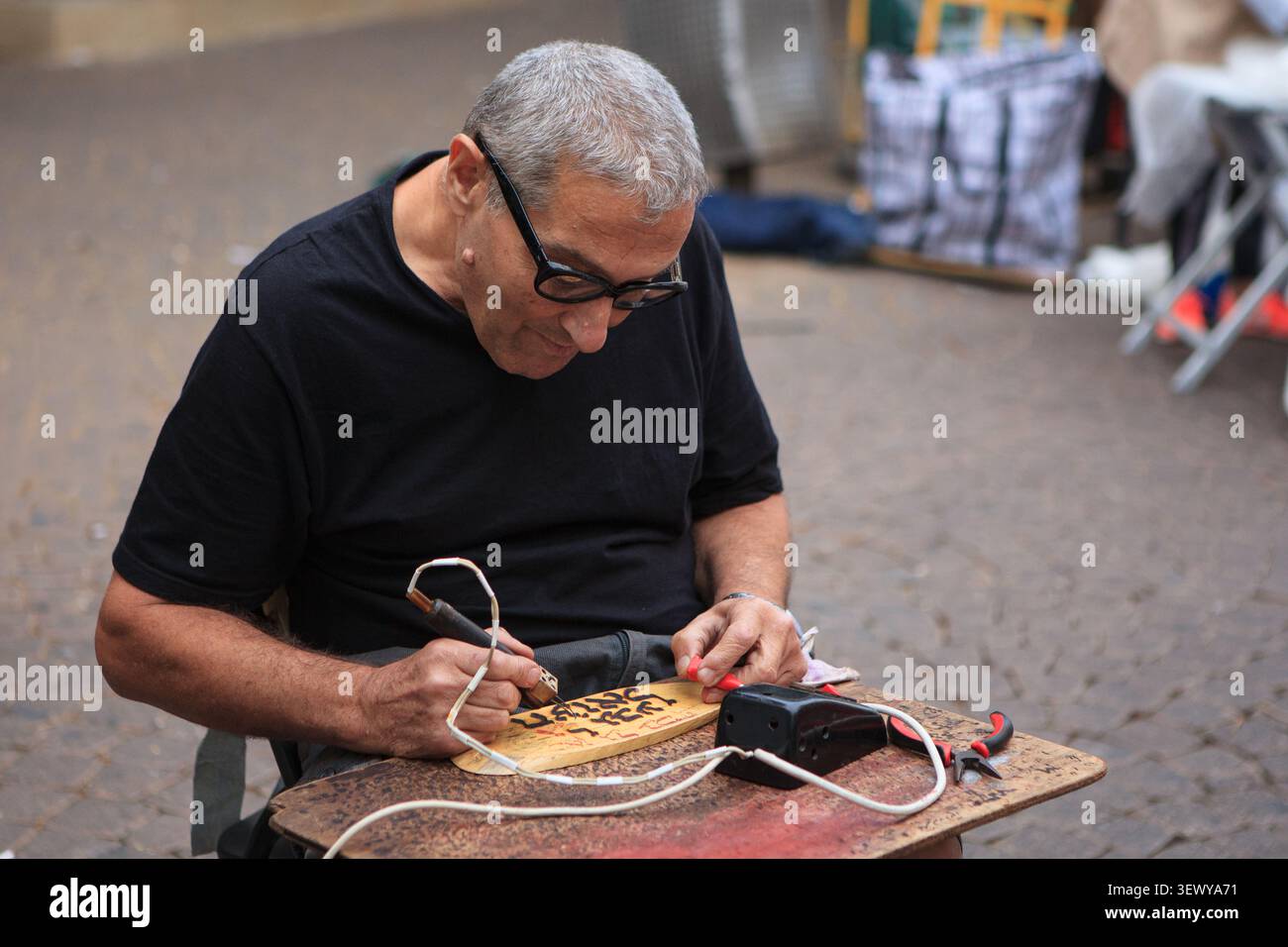 TEL AVIV, ISRAEL, 29. November 2013: Ein Handwerker verbrennt hebräischen Text auf eine hölzerne Tafel mit einem yrographischen Werkzeug an seinem Stand in der Nachalat Binyamin Street Stockfoto