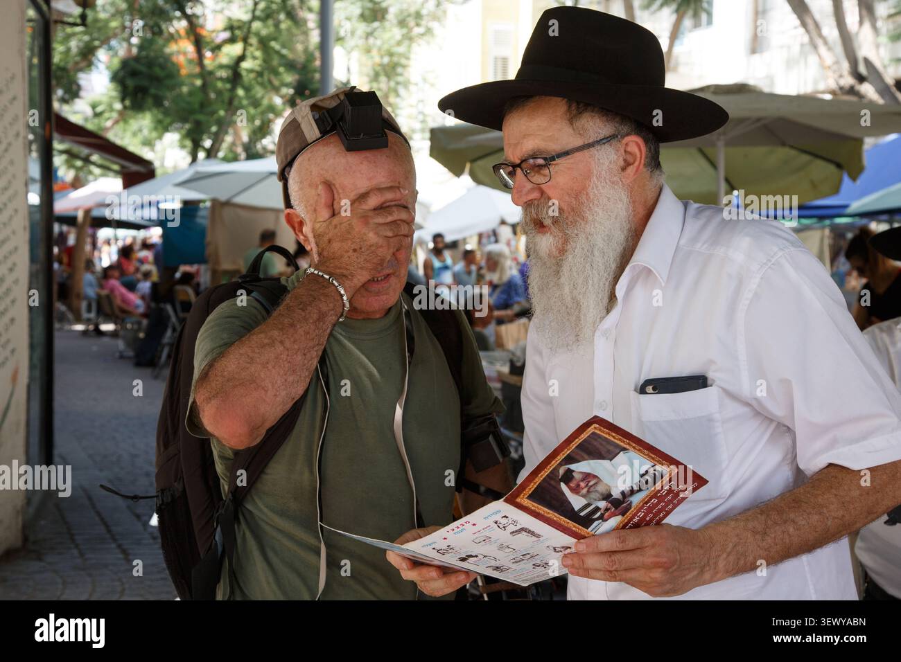 TEL AVIV, ISRAEL – 20. Juni 2018: Ein säkularer jüdischer Mann mit Tefillin betet zusammen mit einem orthodoxen jüdischen Mann auf dem Nachalat Binyamin Street Market Stockfoto