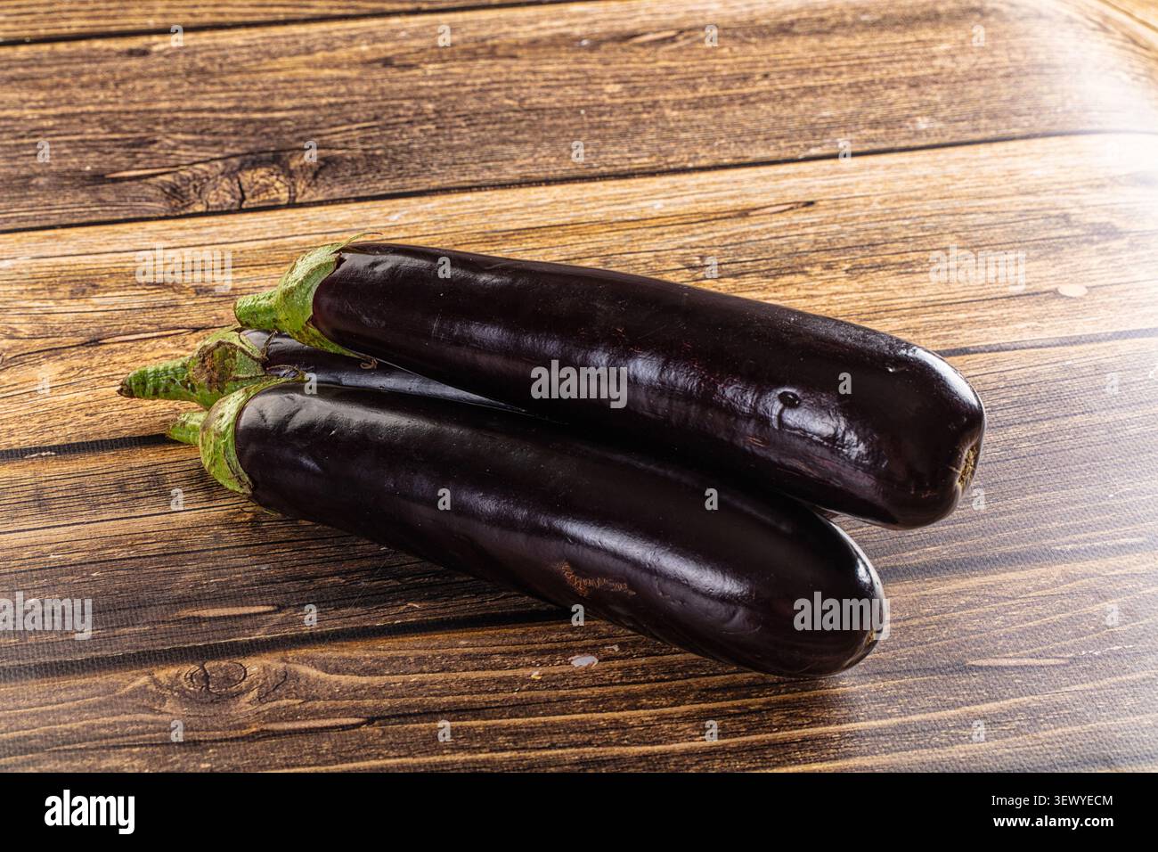 Drei frische lila Auberginen auf rustikalem Holzhintergrund. Minimalistische Komposition mit Kopierraum für Text. Konzept für gesunde Ernährung, vegane Ernährung, fres Stockfoto