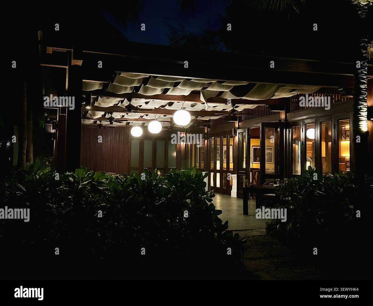 Elegantes Resort Restaurant Terrasse beleuchtet bei Nacht. Eine warme und einladende Außenterrasse am Abend. Stockfoto