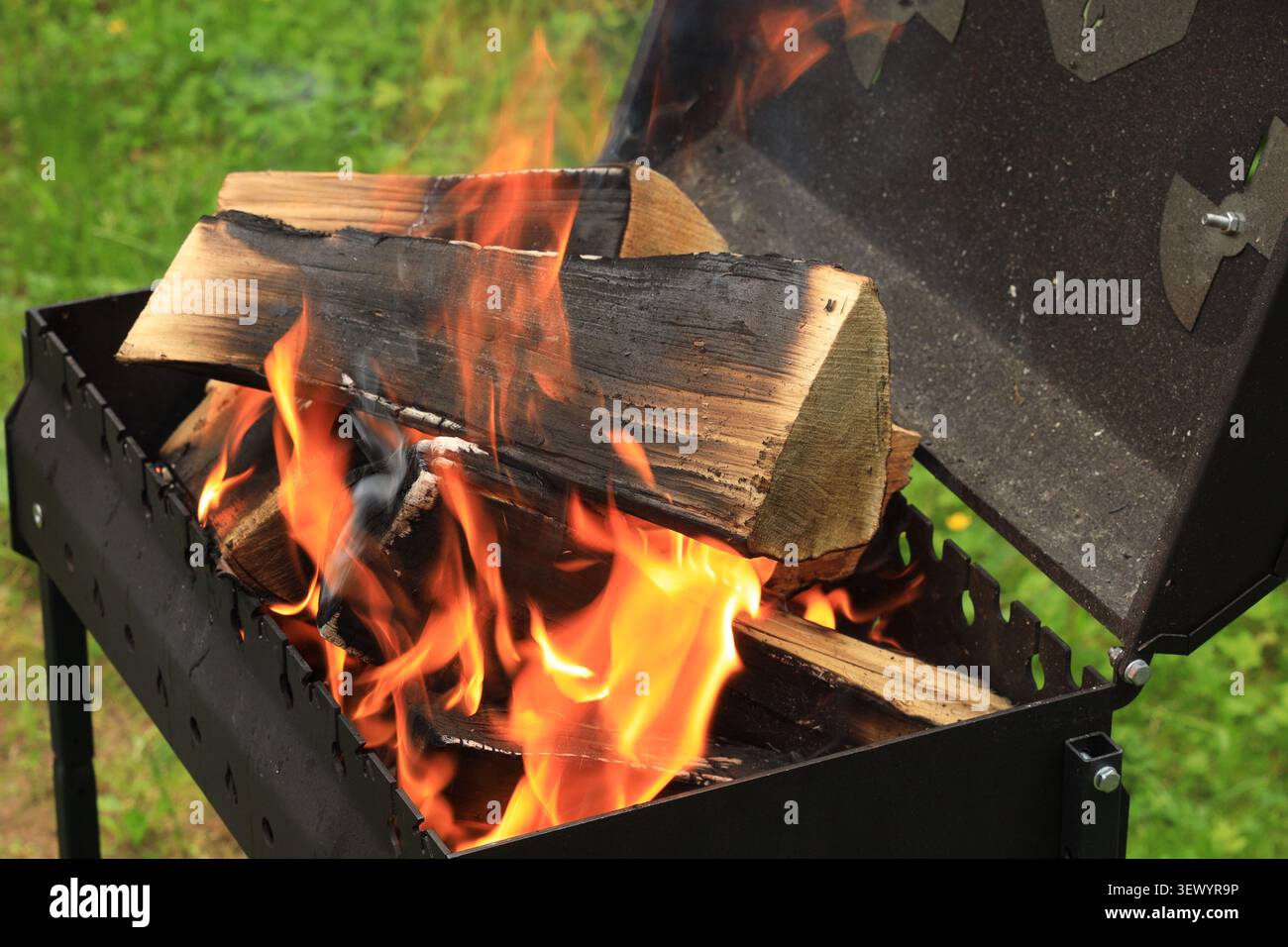 Schwarzer Brazier mit offenem Deckel und brennenden Stämmen und grünem Hintergrund Stockfoto