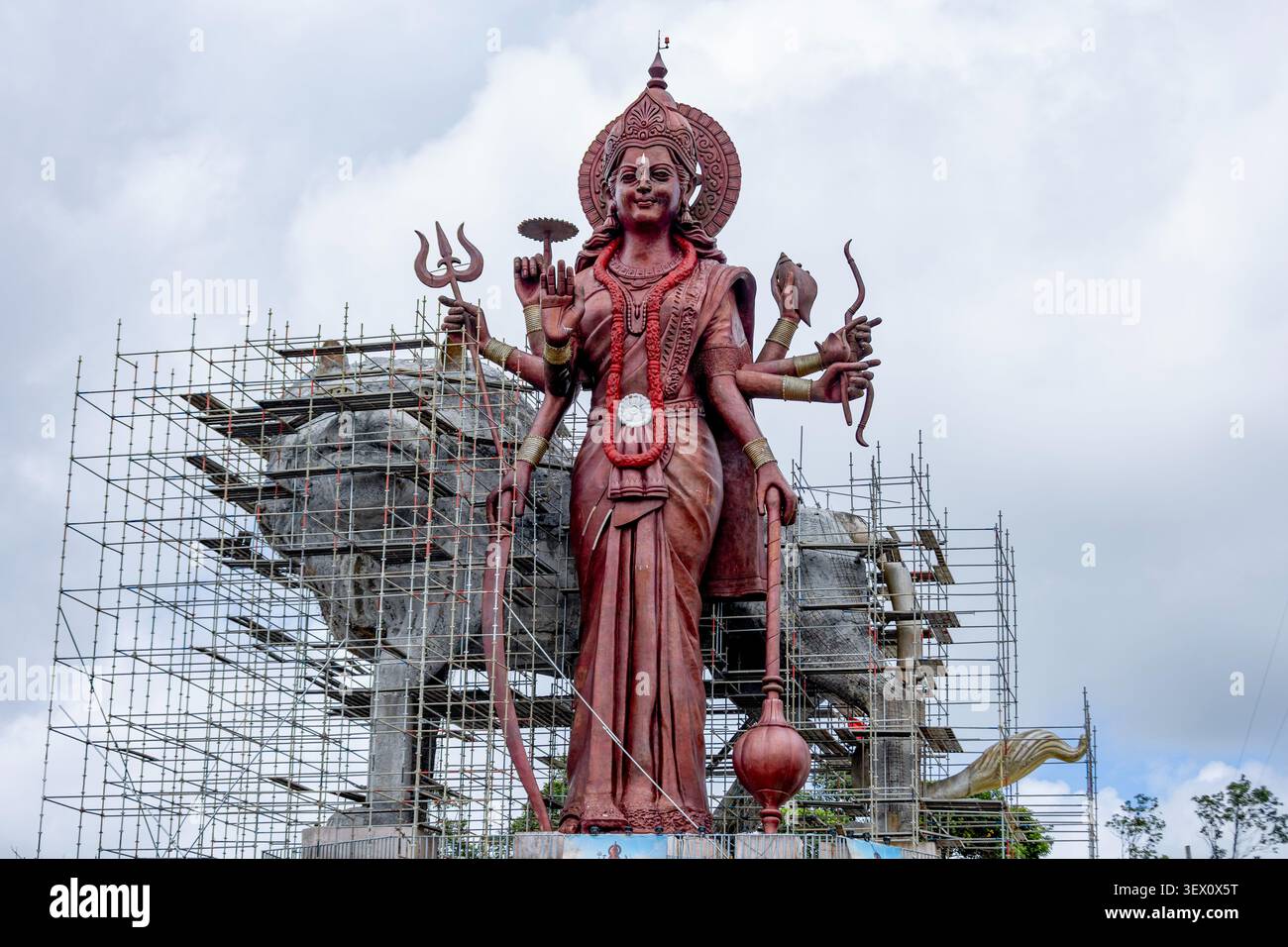 Massive mehrarmige Hindugottin-Statue im Bau mit Gerüsten gegen bewölkten Himmel Stockfoto