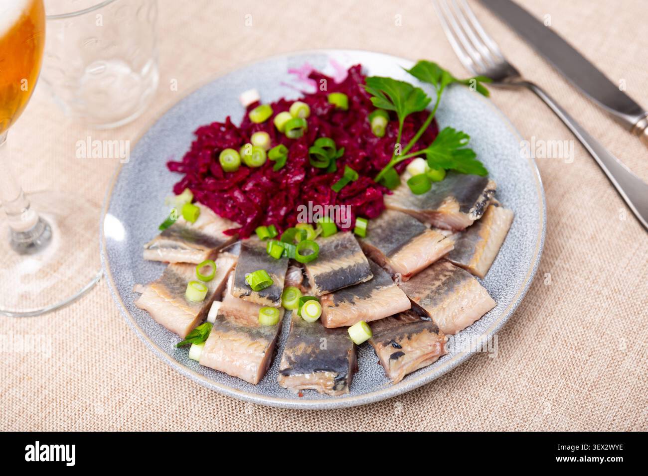 Auf blauen Tellern aus gesalzenem Heringsfilet, verzierter Petersilie und grünen Zwiebeln, mit gedünsteten Rüben Stockfoto