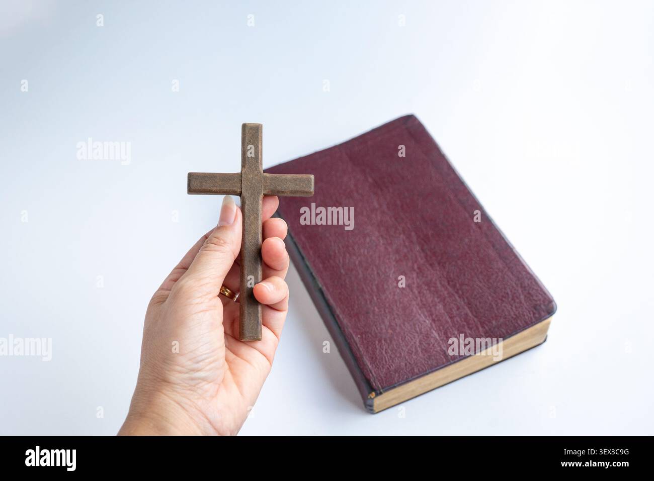 Hand mit einem hölzernen Kruzifix-Kreuz, mit einer Bibel im Hintergrund. Stockfoto