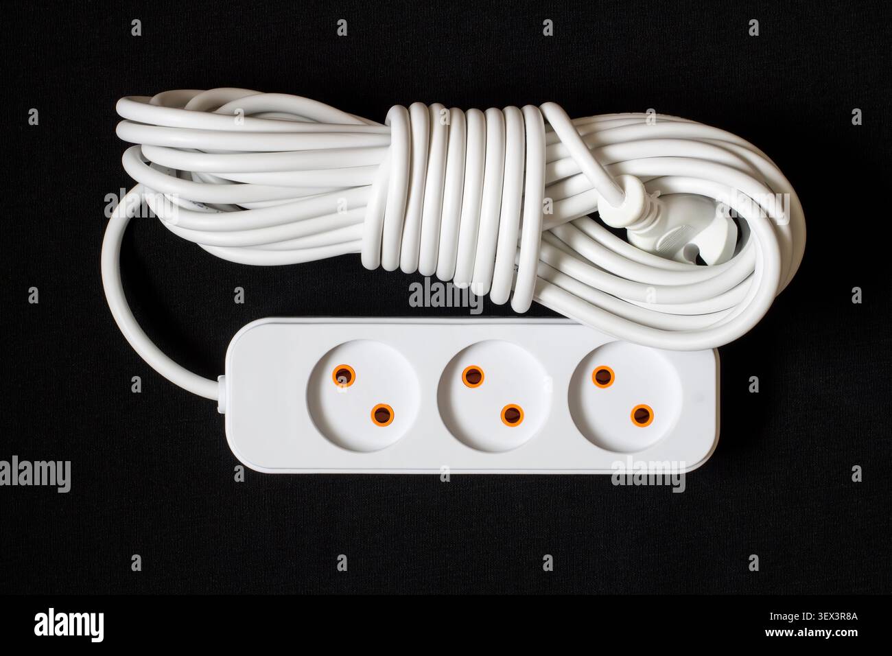 Weißes elektrisches Verlängerungskabel auf dunklem Hintergrund. Langes Elektrokabel mit Steckdosen. Stockfoto