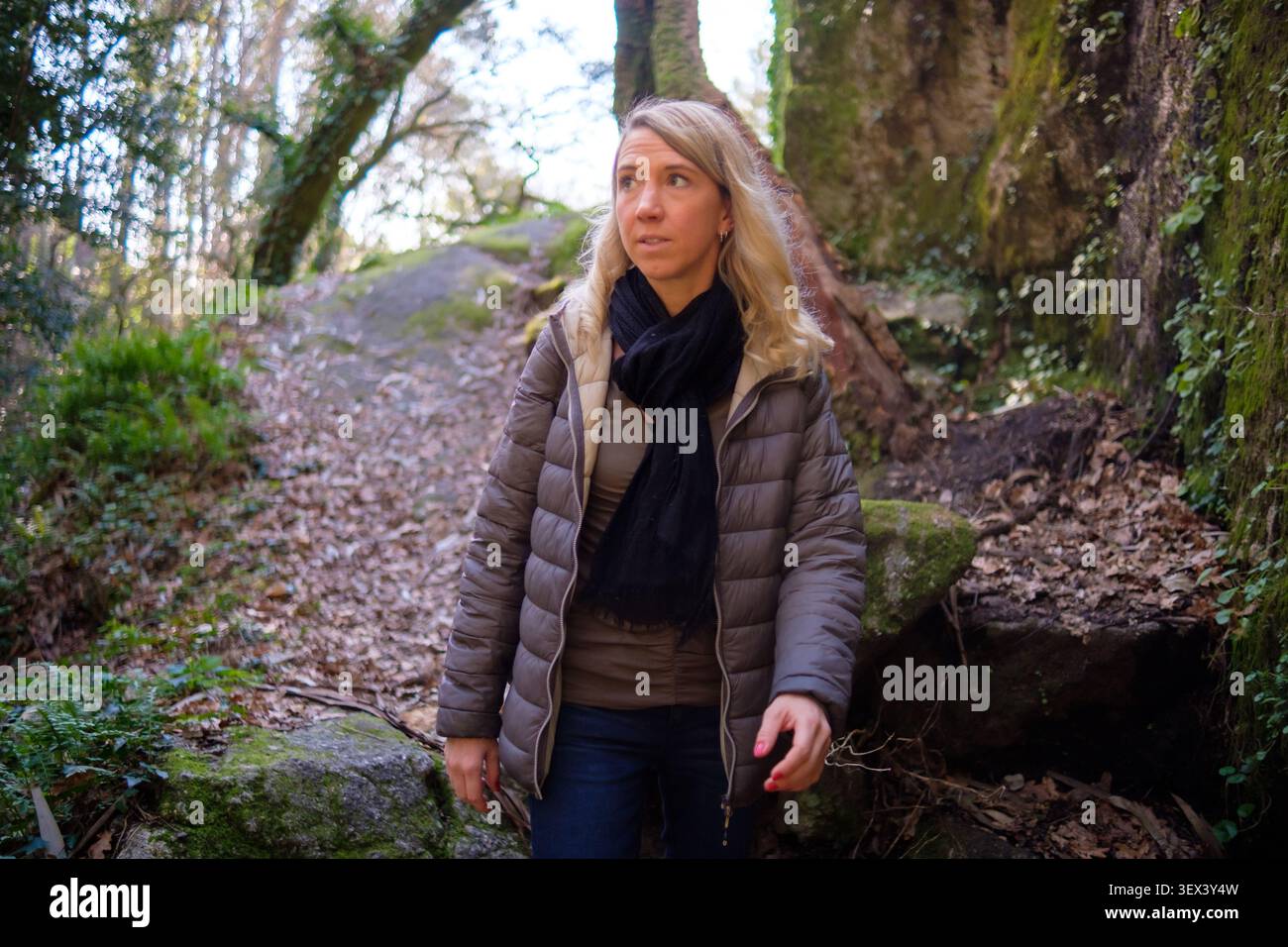 Blonde Frau, die einen Waldweg erforscht, umgeben von Bäumen und moosigen Felsen Stockfoto