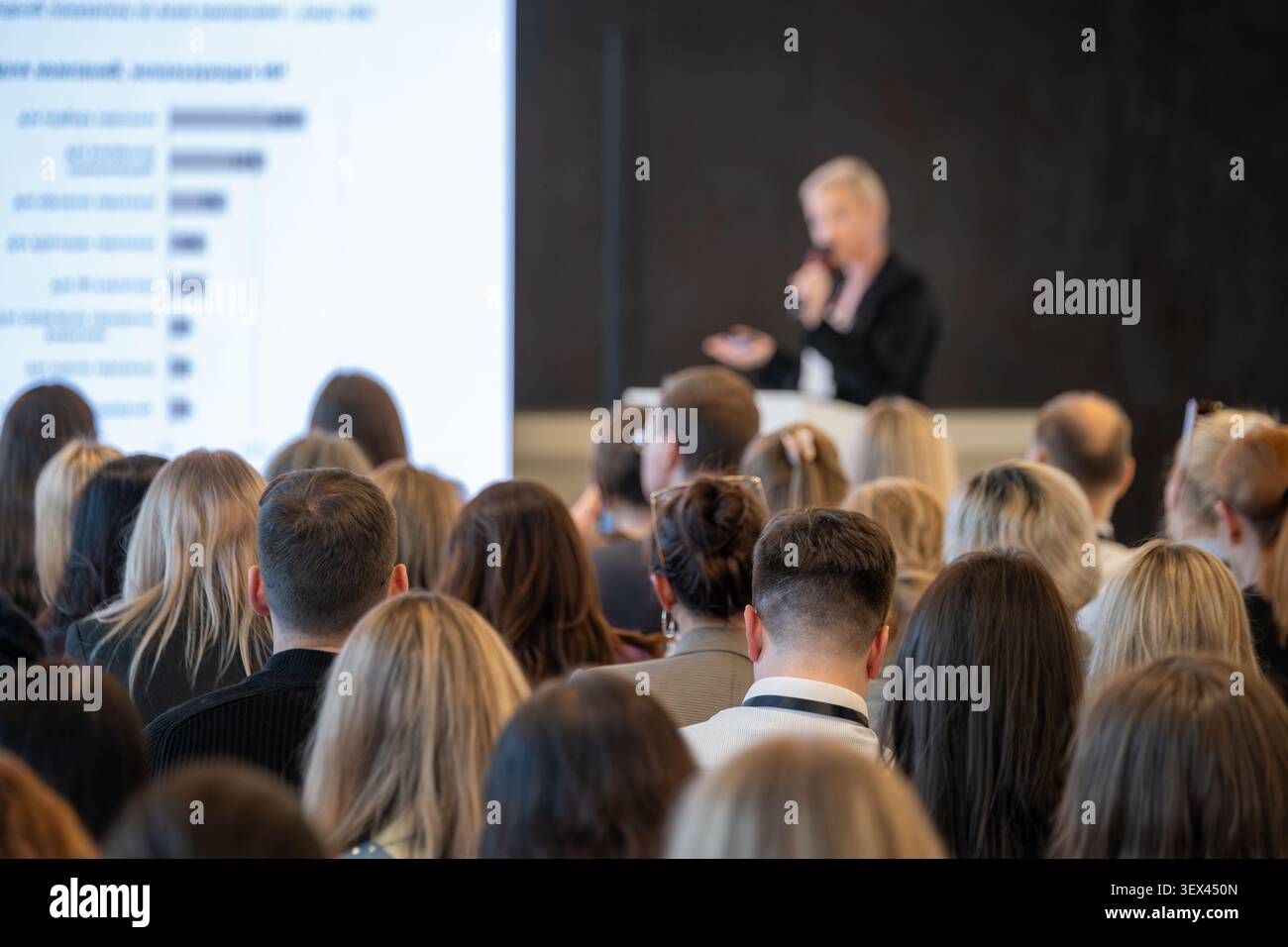 Das Publikum der Unternehmenskonferenz hört dem Referenten zu, konzentriert sich auf die Teilnehmer, verschwimmt den Sprecher und die Folie. Stockfoto