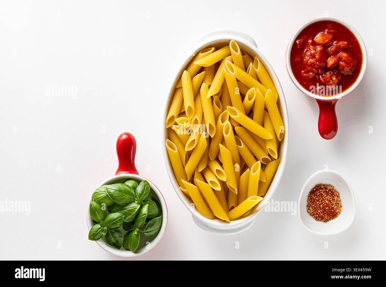 Ungekochte Penne-Pasta in weißer Auflaufform mit frischer Basilikum-Tomatensauce und Gewürz auf sauberem weißem Hintergrund Stockfoto