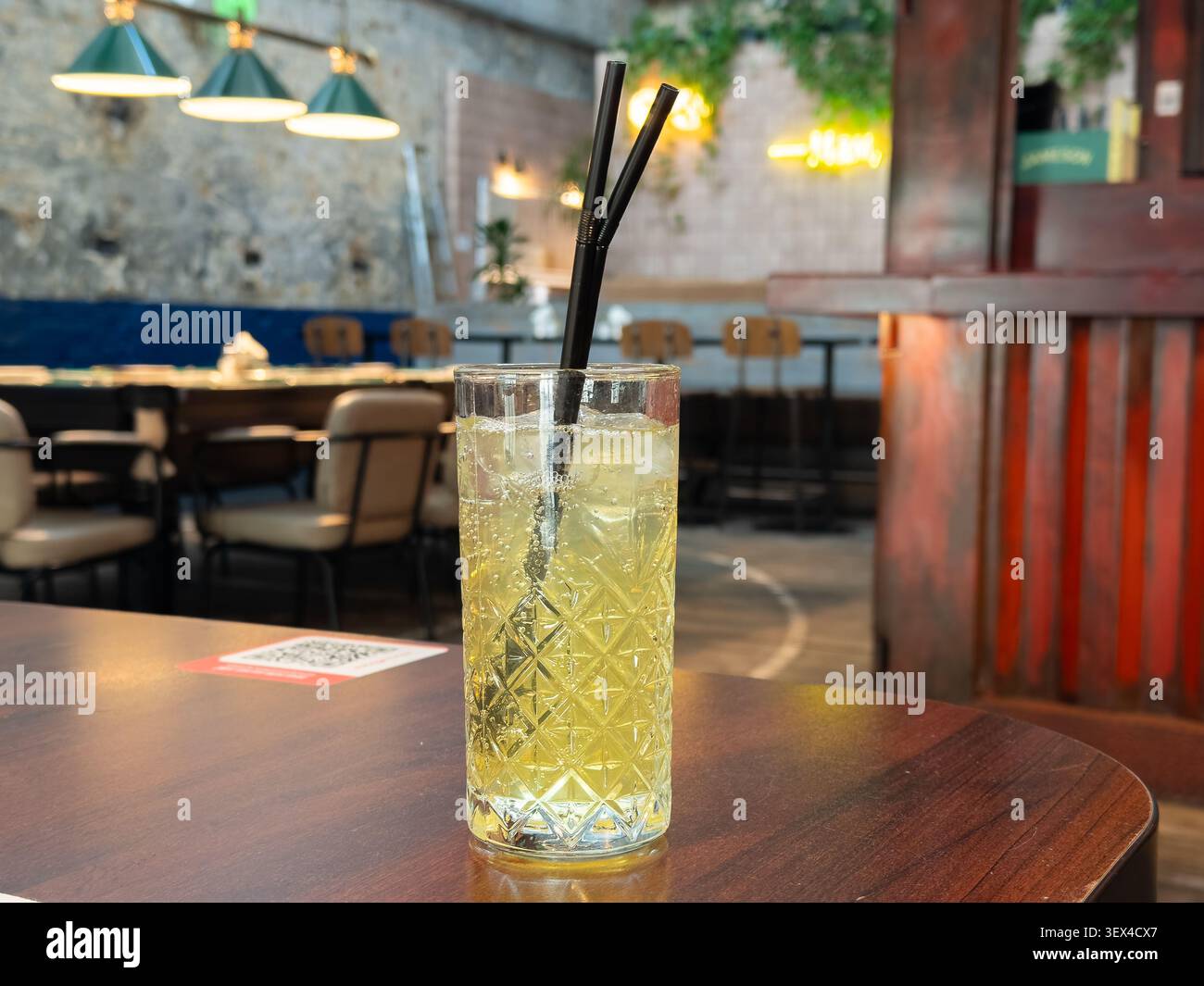 Erfrischendes alkoholisches Eisgetränk, serviert in einem Vintage-Tumbler mit Muster auf einem Tisch, der die lebhafte und gemütliche Stimmung eines Abends in dunkler Beleuchtung einfängt Stockfoto