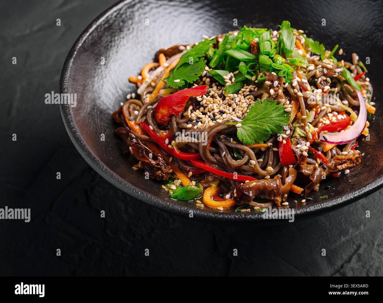 Soba-Nudeln in einer schwarzen Schüssel vor dunklem Betonhintergrund anbraten Stockfoto