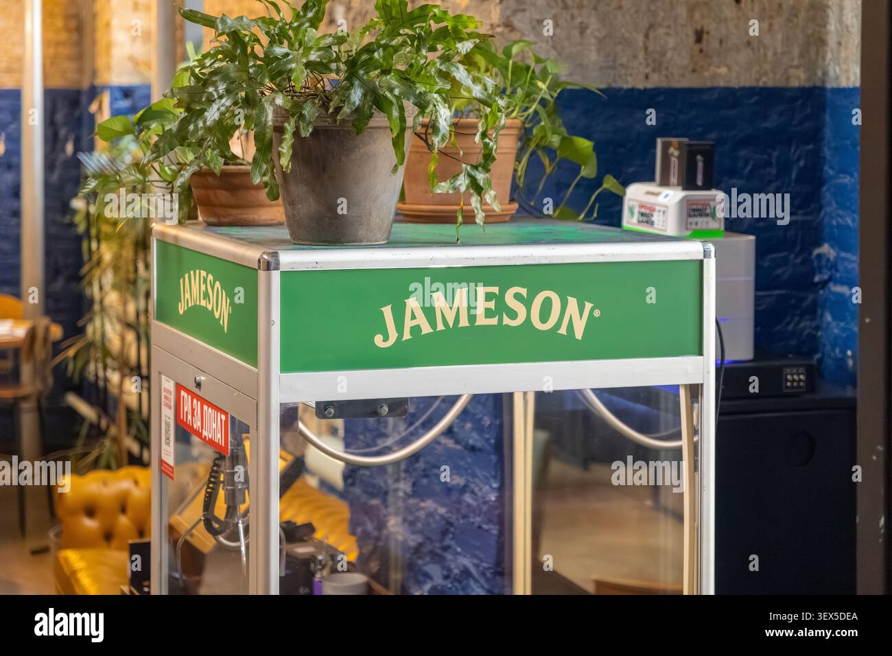 Kiew, Ukraine - 21. März 2026: Jameson Werbekran-Klauenspielmaschine mit Innenpflanzen dekoriert in einem zeitgenössischen Pub-Raum für Stockfoto
