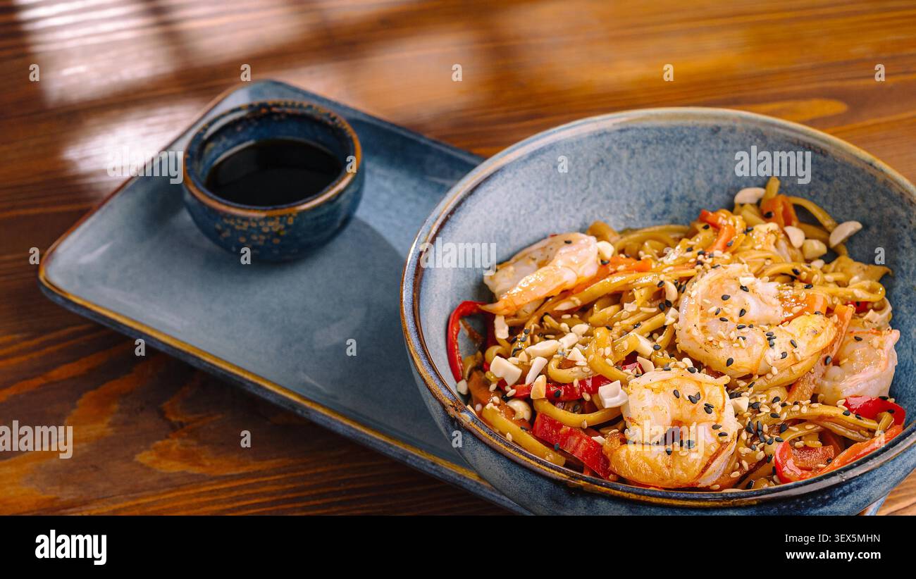 Garnelen-Udon-Nudeln unter Rühren mit Gemüse, Erdnüssen und Sesamsamen neben Sojasauce Stockfoto