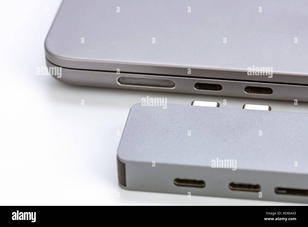 Nahaufnahme eines silbernen USB-Typ-C-Hub-Adapters aus Aluminium mit zwei Anschlüssen neben einem modernen Laptop mit Thunderbolt-Anschlüssen und SD-Karten-Slo Stockfoto