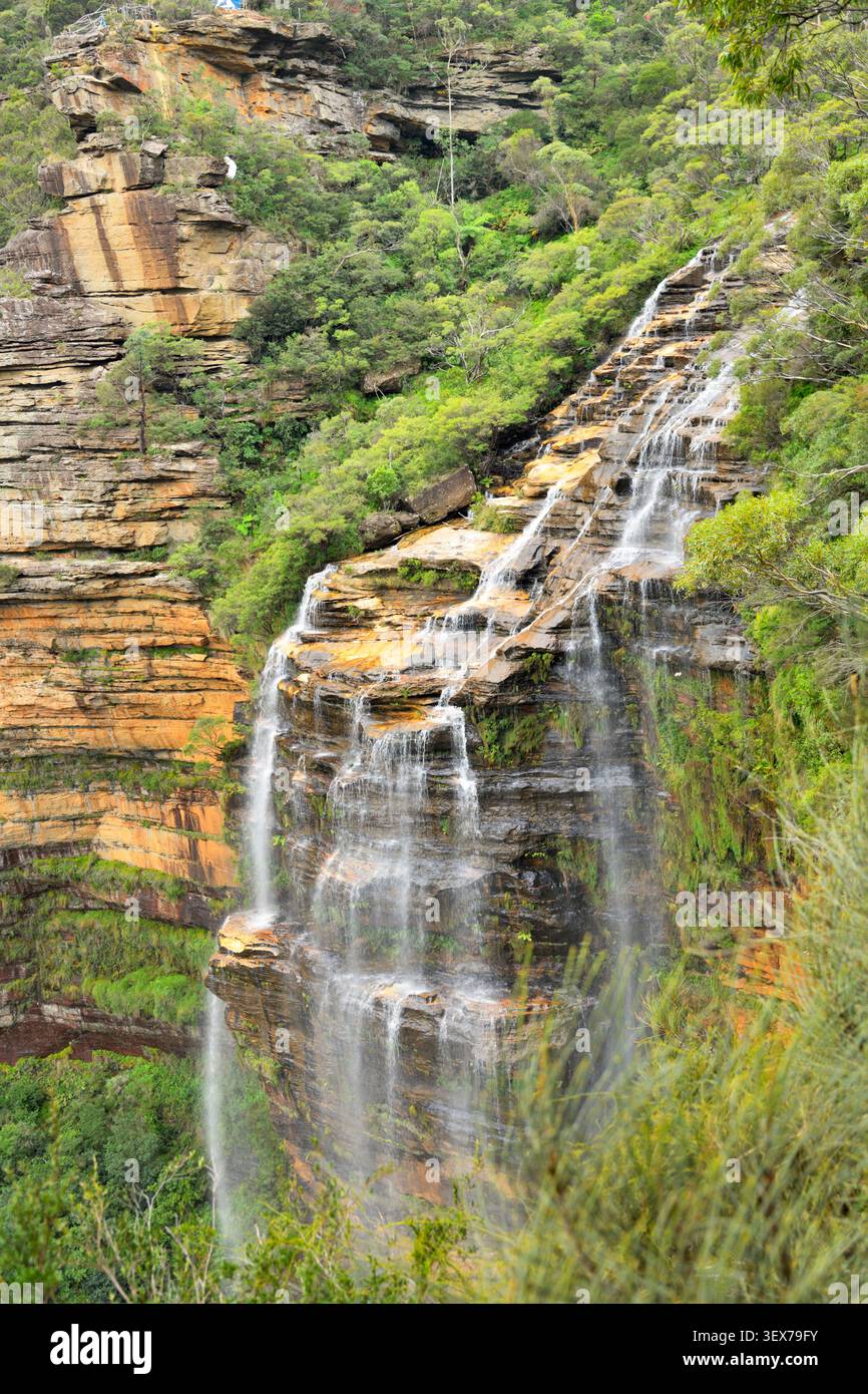 Australien, New South Wales, Wentworth Falls, Blue Mountains National Park, Wentworth Falls Wasserfall, Wasserfall, der durch eine Sandsteinklippe in Buschvegetation fließt Stockfoto